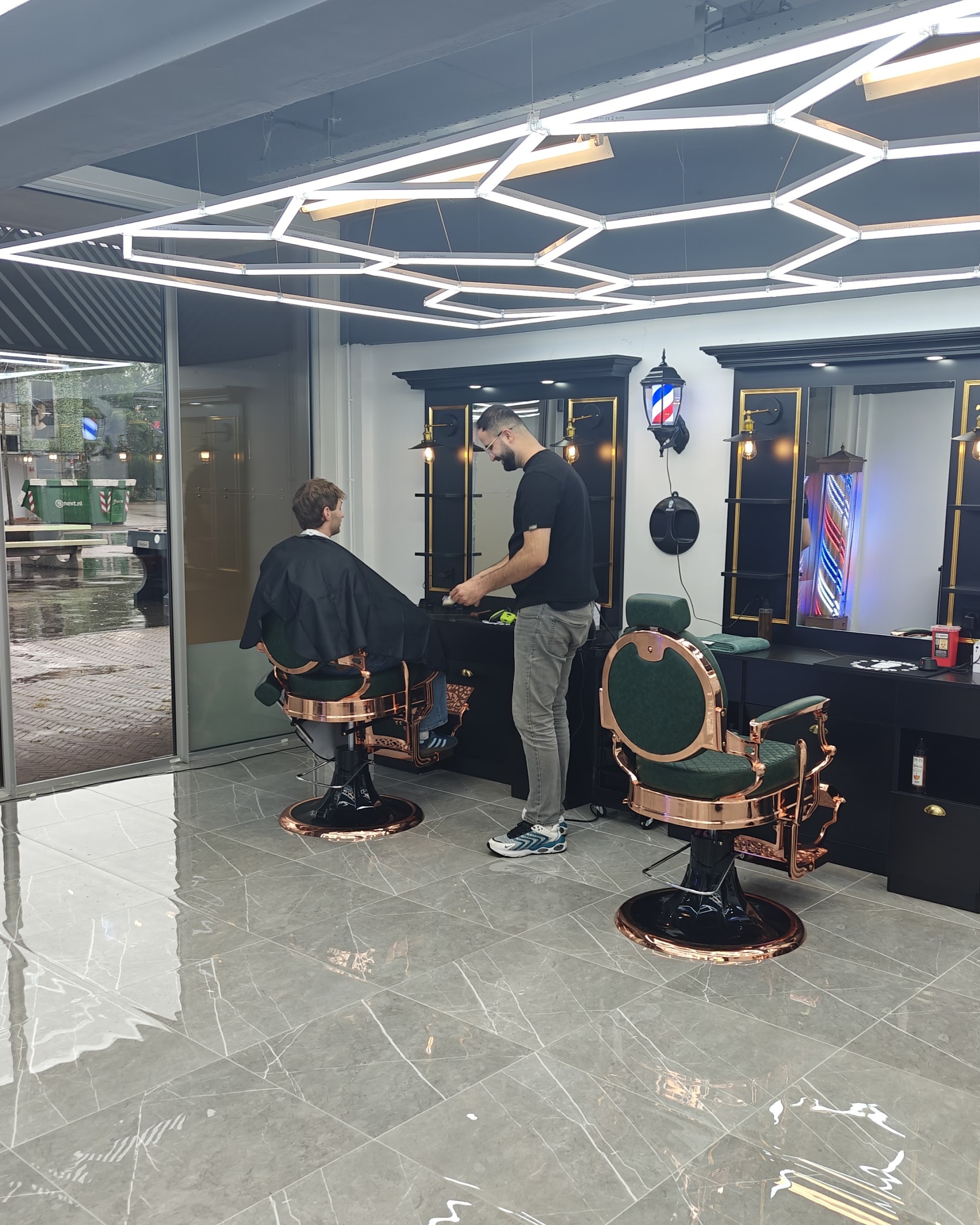 Een kapper aan het werk bij een klant in de salon, onder het zeshoekige lichtplafond